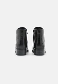 Botas negras de cuero hasta el tobillo con una textura suave, que cuentan con un cierre de cremallera en la parte trasera y un tacón bajo apilado.