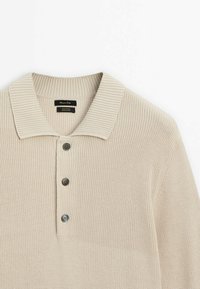 Polo en coton beige tricoté avec col côtelé et trois boutons foncés sur le devant.