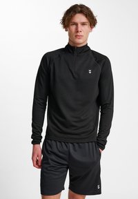 Zwarte longsleeve met rits, van textuurstof en met een klein logo op de borst. Gecombineerd met donkere shorts, beide ontworpen voor sportkleding.