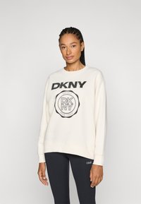 Felpa crema con logo "DKNY" nero ed emblema circolare. Vestibilità ampia, scollatura tonda, tessuto a trama. Leggings neri con branding.