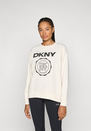 Sudadera cremosa con logo negro "DKNY" y emblema circular. Corte relajado, cuello redondo, tela texturizada. Leggings negros con marca.