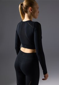 Schwarzes sportliches Crop-Top und Leggings mit strukturierten Netzpaneelen und Ausschnitten. Figurbetontes Design mit langen Ärmeln und hohem Bund.