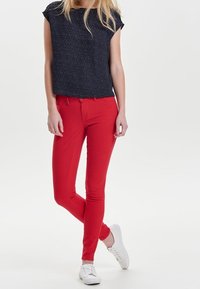 Haut à manches courtes bleu marine avec motif, associé à un pantalon slim rouge et des baskets blanches. La tenue présente une coupe décontractée et des couleurs vives.
