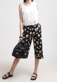 Blouse blanche sans manches avec un détail en volants, associée à des culottes noires à motifs floraux. Un sac à main noir et des sandales plates complètent la tenue.