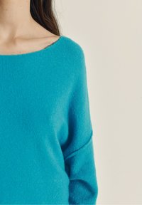 Turkis strikket sweater med bred bådhals, lange ærmer og blød tekstur, med lette faldne skuldersømme.