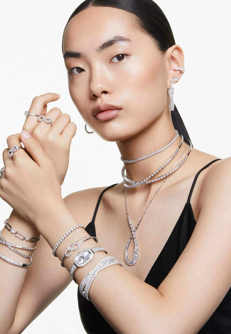 Silversmycken som inkluderar ringar, armband, en klocka och ett halsband med intrikata mönster. Släta ytor och glittrande detaljer över hela smyckena.