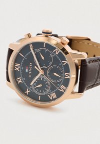 Orologio da polso rosa oro con quadrante nero, numeri romani, tre sottodial per giorno, data, ora 24 e cinturino in pelle marrone.