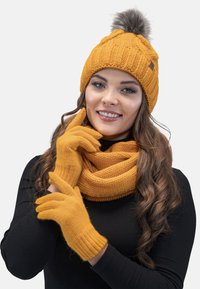 Sininen neulepipo, jossa on pom-pom, yhteensopiva huivi ja hanskat. Tekstuuriinen palmikkoneulekuvio; pehmeä materiaali; tiukka istuvuus.