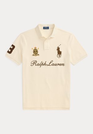 Polo crème avec inscription Ralph Lauren, logo joueur de polo brodé, numéro 3 sur la manche et blason avec couronne sur la poitrine.