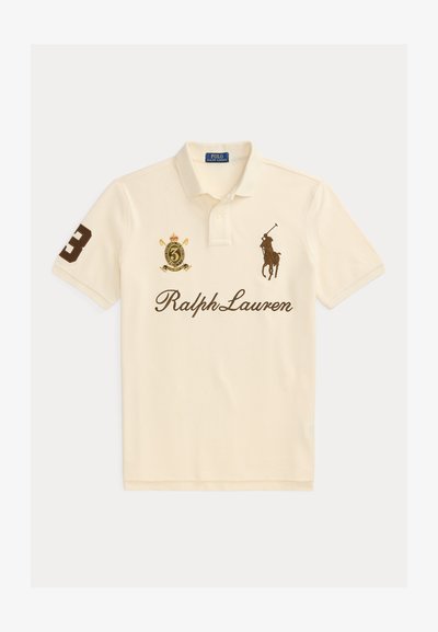 Κρεμ πόλο μπλούζα με την υπογραφή Ralph Lauren, κεντημένο λογότυπο παίκτη πόλο, αριθμός 3 στο μανίκι και έμβλημα με κορώνα στο στήθος.