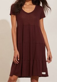 Robe maroon à manches courtes, longueur genou, en tissu texturé, avec un col en V, un design à étages et une petite étiquette de marque en bas.