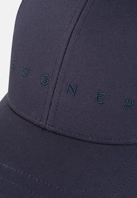Navy baseball cap with textured fabric, featuring raised navy lettering "BOGNER" on the front. Curved brim and stitched detailing.