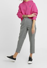 Růžová mikina s kapucí a logem, kalhoty s černobílým houndstooth vzorem a černé tenisky s bílými podrážkami.