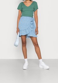 Zielony prążkowany top z krótkimi bufkami, zestawiony z niebieską spódnicą w stylu wrap, pokrytą białym kwiatowym wzorem i falbaniastym dołem. Białe sneakersy na platformie.