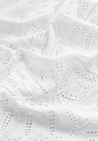 Witte geborduurde stof met intricat uitgesneden patronen, delicate texturen en geschulpte randen. Ideaal voor lichte kleding of decoratie.