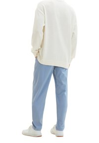Biały sweter z dzianiny z opadającymi ramionami, w połączeniu z jasnoniebieskimi, luźno dopasowanymi spodniami. Białe trampki z teksturowaną powierzchnią i gumową podeszwą.