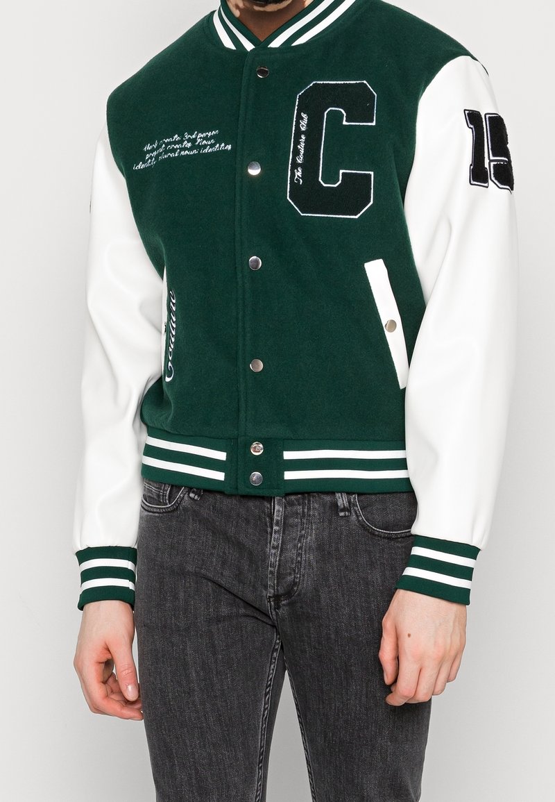 Giacca varsity verde con maniche bianche, bottoni a pressione metallici e dettagli ricamati. Presenta polsini e fascia inferiore a righe; design casual.