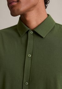 Roheline puuvillane särk struktureeritud kraega, millel on roheline nupuvärvel ja pehme tekstuur. Üksikasjalik vaade kaela piirkonnale.