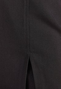 Tessuto nero con una texture liscia, caratterizzato da una cucitura e un piccolo dettaglio con spacco, focalizzato su linee pulite e design minimal.