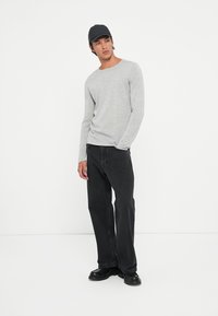 Une chemise grise à manches longues, un jean noir et une casquette noire. La tenue présente un ajustement décontracté avec un design simple et un tissu texturé.