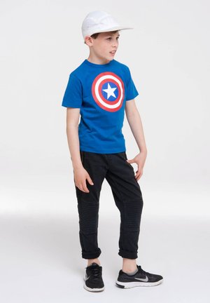 Blue cotton t-shirt featuring a large red and white circular graphic with a blue star, paired with black pants with ribbed texture and black sneakers.