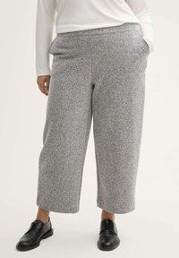 Pantalones de patrón de espiga gris con un ajuste relajado, pierna ancha y bolsillos, combinados con zapatos negros de cordones. Tejido suave y texturado.