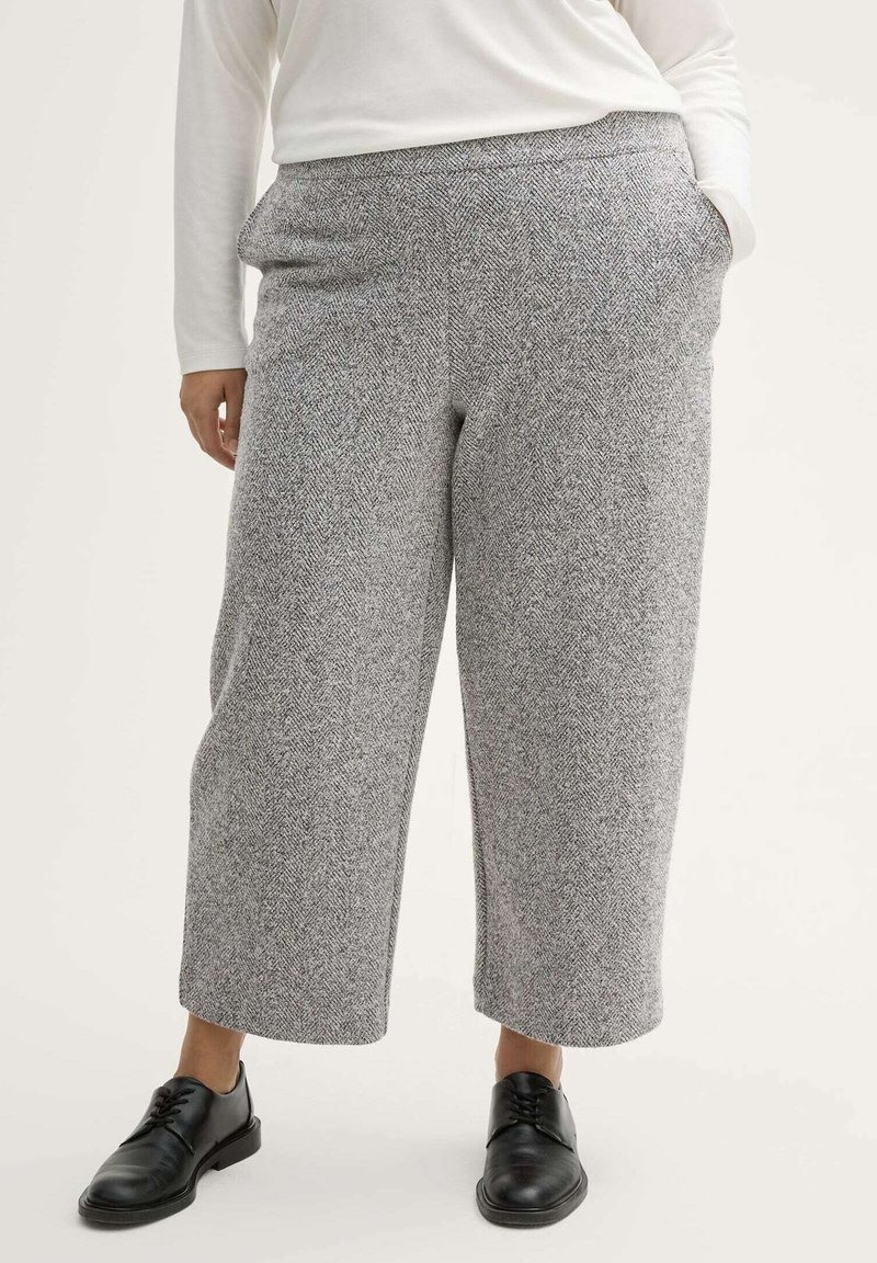 Pantalones de patrón de espiga gris con un ajuste relajado, pierna ancha y bolsillos, combinados con zapatos negros de cordones. Tejido suave y texturado.