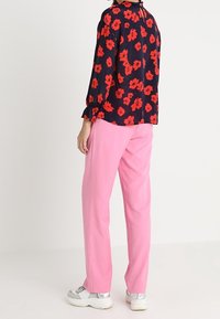 Blusa floreale con design rosso e nero, abbinata a pantaloni dritti rosa chiaro. Calzature con suola bianca e accenti metallici.