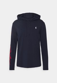 Tmavě modrá mikina s dlouhým rukávem vyrobená z bavlny, s logem na přední straně a červeným dekorativním potiskem na levém rukávu. Kapuce se šňůrkou.