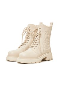 Beige nahkateksaskengät paksulla pohjalla, joissa on teksturoitu ruusukuosi sivussa ja perinteiset nauhat.