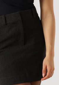 Schwarzer Wollmischrock mit tailliertem Schnitt, flacher Vorderseite, seitlichen Taschen und glatter Textur, der bis zur Mitte des Oberschenkels reicht.