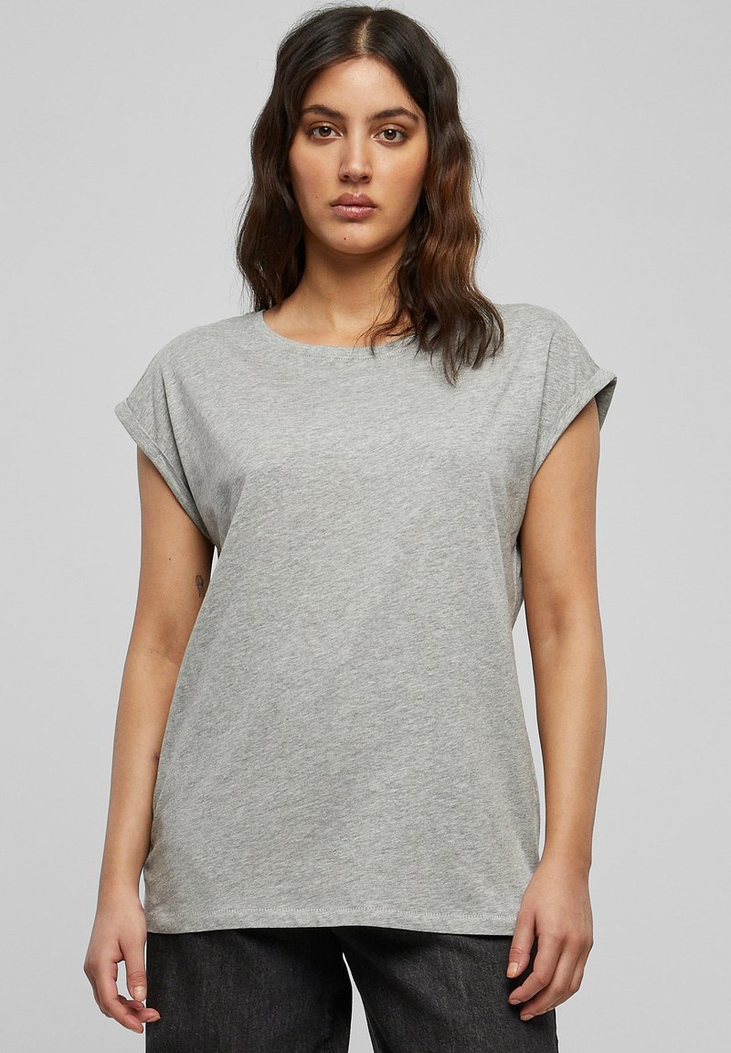 Maglietta grigia a maniche corte con maniche arrotolate, scollo tondo e tessuto morbido e liscio. Vestibilità ampia, abbinata a pantaloni scuri.