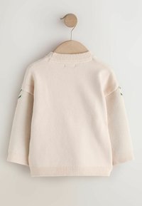Lyserød strikket sweater med ribbet rund hals og teksturerede ærmer. Har broderede detaljer på begge skuldre. Hænger på en træbøjle.