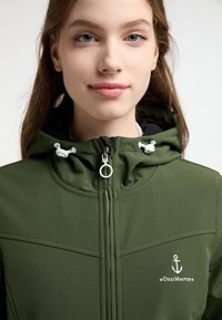 Grøn zip-up jakke med hætte, lavet af glat stof. Har hvide snoretræk og et ankerlogo på brystet.