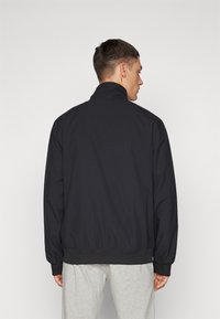 Chaqueta bomber negra con cuello alto, puños acanalados y dobladillo elástico. Fabricada en un tejido liso, presenta un diseño sencillo y limpio sin adornos.