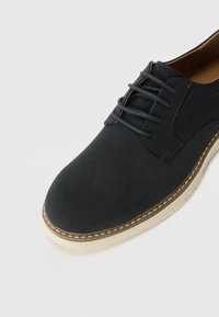 Schwarzer Lederschuh mit glatter Textur, runder Spitze und dekorativen Nähte. Verfügt über graue Schnürsenkel und eine cremefarbene Sohle.
