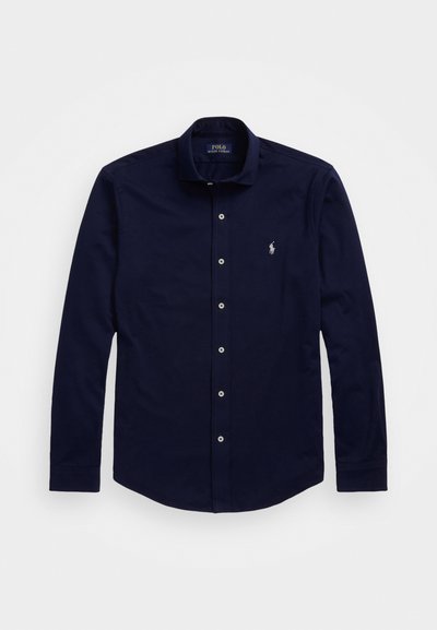 Hosszú ujjú tengerészkék pólóing, klasszikus gallérral, gombos záródással, hímzett logóval a mellkason, és sima pamutszerkezettel.