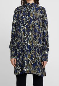 Camicia a maniche lunghe in un tessuto scuro con un motivo astratto multicolore di verdi, blu e gialli. Design con colletto, vestibilità rilassata.
