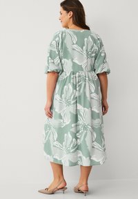 Groene bloemenjurk met witte patronen, korte pofmouwen, elastische tailleband, lengte tot halverwege de kuit, gecombineerd met lichtbruine sandalen met hak.