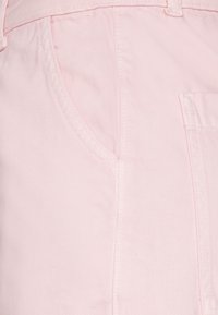 Tecido de denim cor-de-rosa com uma textura suave, apresentando um bolso frontal e costura nas laterais. Elementos de design simples e funcionais visíveis.