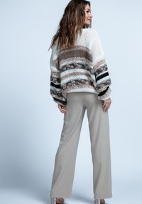 Sweter z dzianiny w kolorze białym, beżowym i czarnym, z paskowanym wzorem, z szerokimi rękawami. W zestawie ze spodniami w jasnym beżu o szerokich nogawkach.