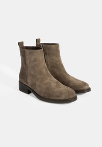 Bottines en daim marron avec une pointe arrondie et des détails de fermeture éclair. Design à talon bloc avec des languettes pour un enfilage facile. Texture lisse.