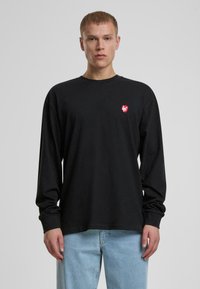 Schwarzes Langarm-T-Shirt mit einem kleinen roten Grafikdesign auf der linken Brust. Hergestellt aus weichem Stoff mit lockerer Passform und Rundhalsausschnitt.