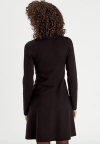 Black long-sleeve dress with a fitted bodice and flared skirt, made of soft fabric, featuring a seam detailing at the waist.