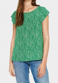 Top verde a maniche corte con un motivo zigrinato bianco, caratterizzato da un collo a giro e una silhouette morbida, abbinato a jeans in denim blu.