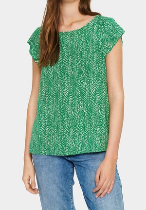 Top verde a maniche corte con un motivo zigrinato bianco, caratterizzato da un collo a giro e una silhouette morbida, abbinato a jeans in denim blu.