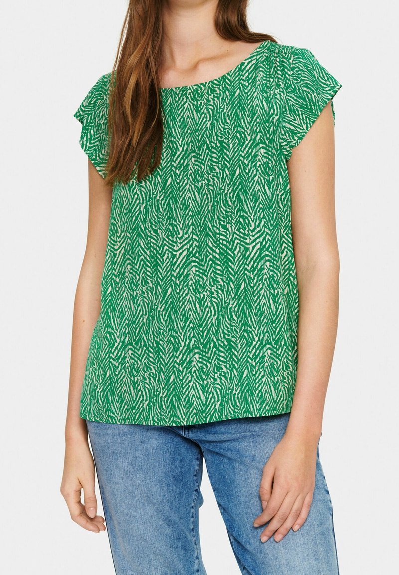Top verde a maniche corte con un motivo zigrinato bianco, caratterizzato da un collo a giro e una silhouette morbida, abbinato a jeans in denim blu.