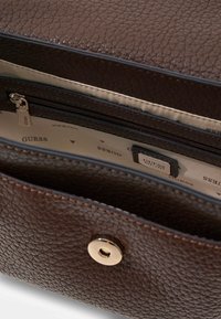 Bruine gestructureerde handtas met een ritssluiting aan de binnenkant, gouden hardware-accenten en een voering met het "GUESS"-logo.