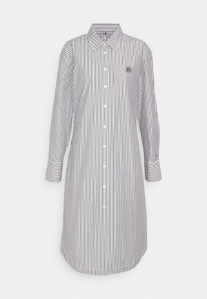 Pruhované šaty v námořní modrej a bielej farbe, so špicatým golierom, zapínaním na gombíky, dlhými rukávmi a malým logom na hrudi.