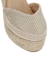 Zapato cuña beige con un upper de tela tejida texturizada y una plataforma de yute trenzado, con punta redondeada y forro interior suave.
